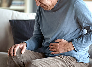 A senior is sat in this photo, holding his stomach suggesting his hernia is causing significant discomfort or even pain.