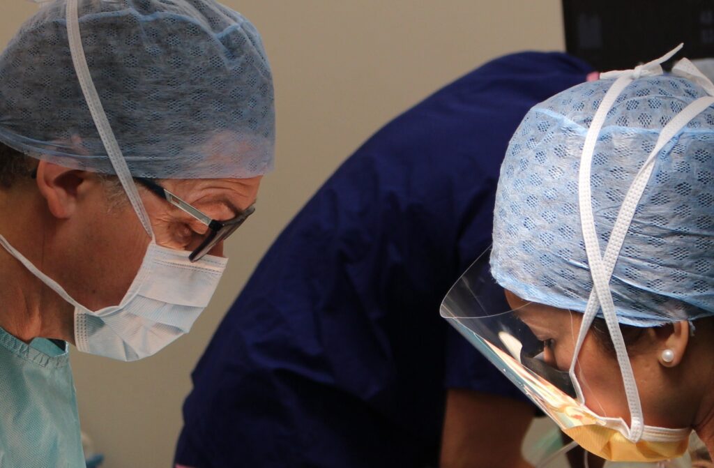 Image showing close up of a male surgeon and female surgical assistant. They are performing hernia surgery using local anaesthetic and sedation, one option for how to repair a hernia.