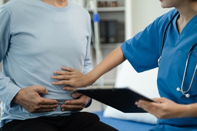 This photo represents an epigastric hernia patient being speaking with a medical professional. His hands are on his abdomen and the doctor is feeling his stomach.