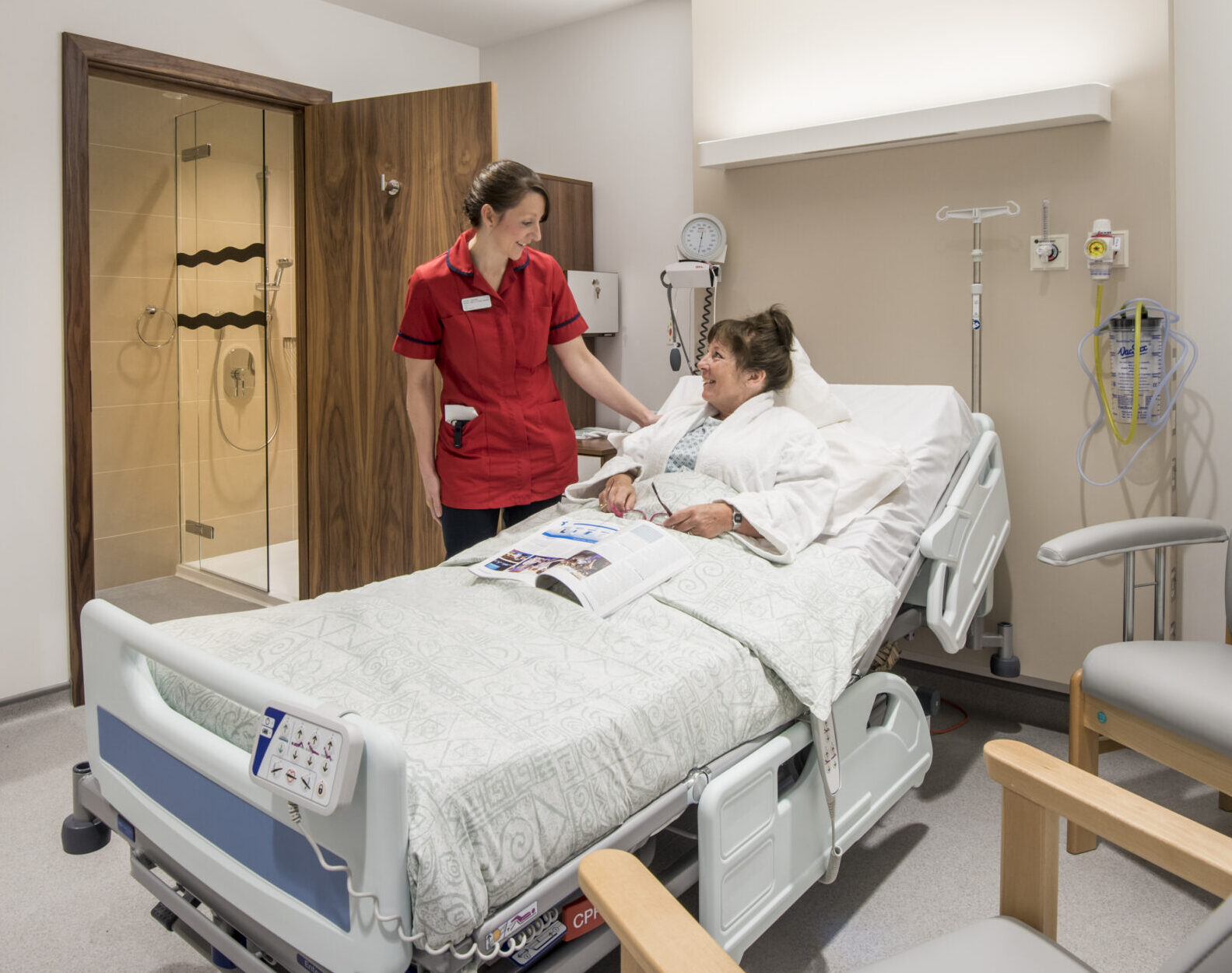 This photo represents a femoral hernia patient in her hospital bed being reassured by a nurse, whose hand rests on the patient's shoulder.