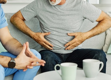 This photo represents a paraumbilical hernia patient being speaking with a medical professional. His hands are on his stomach.