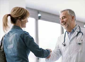 This photo shows a female spigelian hernia patient meeting a surgical-coat-wearing and welcoming consultant surgeon. They are shaking hands.