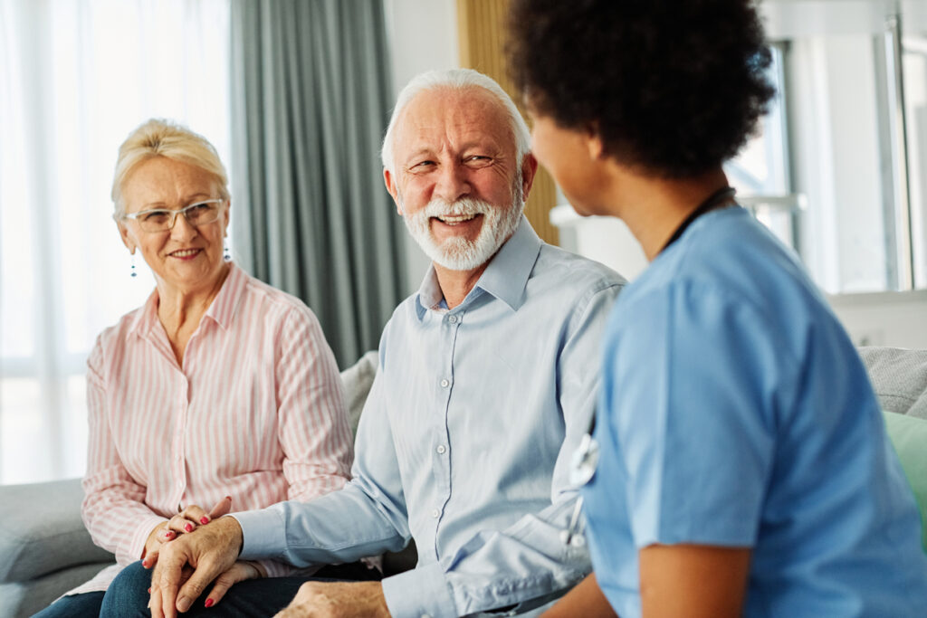 A nurse sitting with a happy senior couple, discussing if hernia surgery is safe for elderly or frail patients.