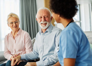 A nurse sitting with a happy senior couple, discussing if hernia surgery is safe for elderly or frail patients.